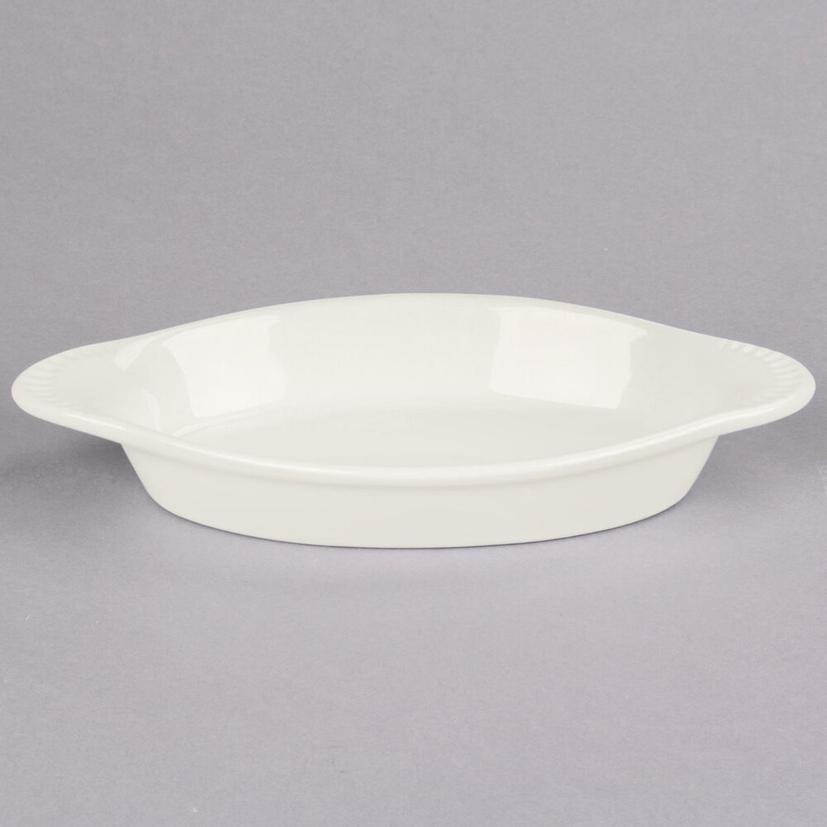 Tuxton BEN-150 17 oz. oval eggshell ceramic Welsh rarebit dish with integrated handles on a gray background