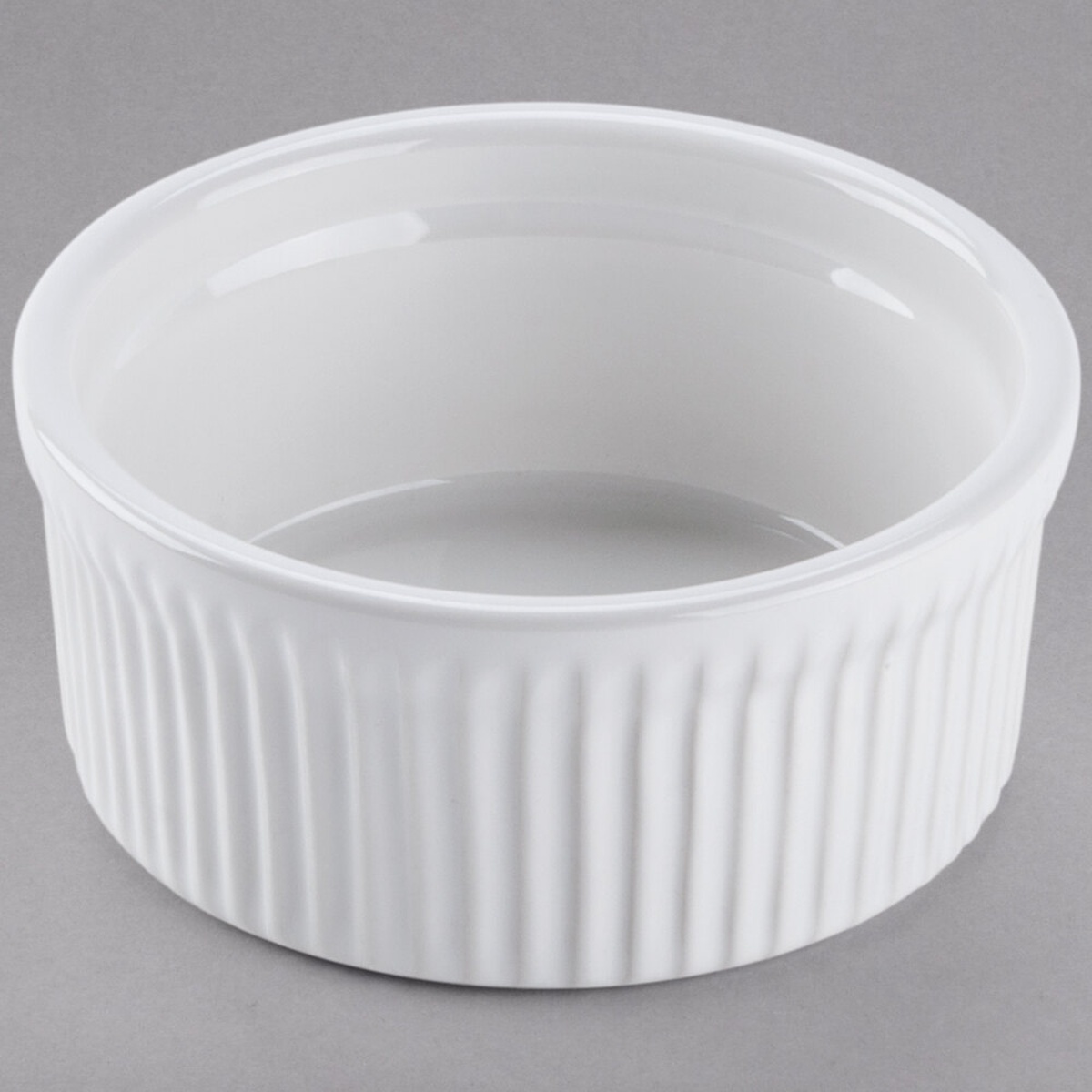 Tuxton BWX-1002 10 oz white fluted china souffle ramekin shown from a slight overhead angle on a gray background