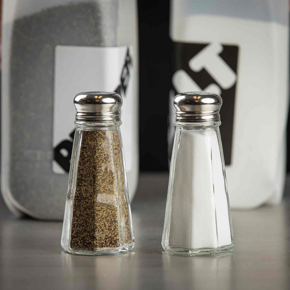 Two TableCraft C156-12 paneled glass shakers filled with salt and pepper displayed on a counter surface