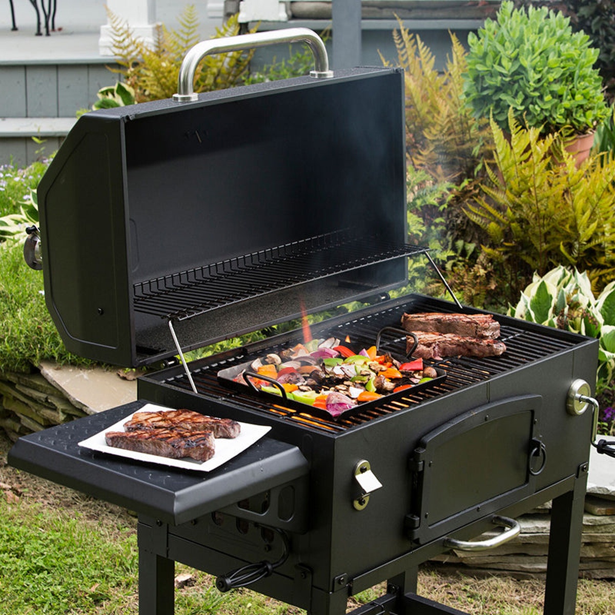 Lodge carbon steel grilling pan in use on an outdoor grill with steaks and vegetables