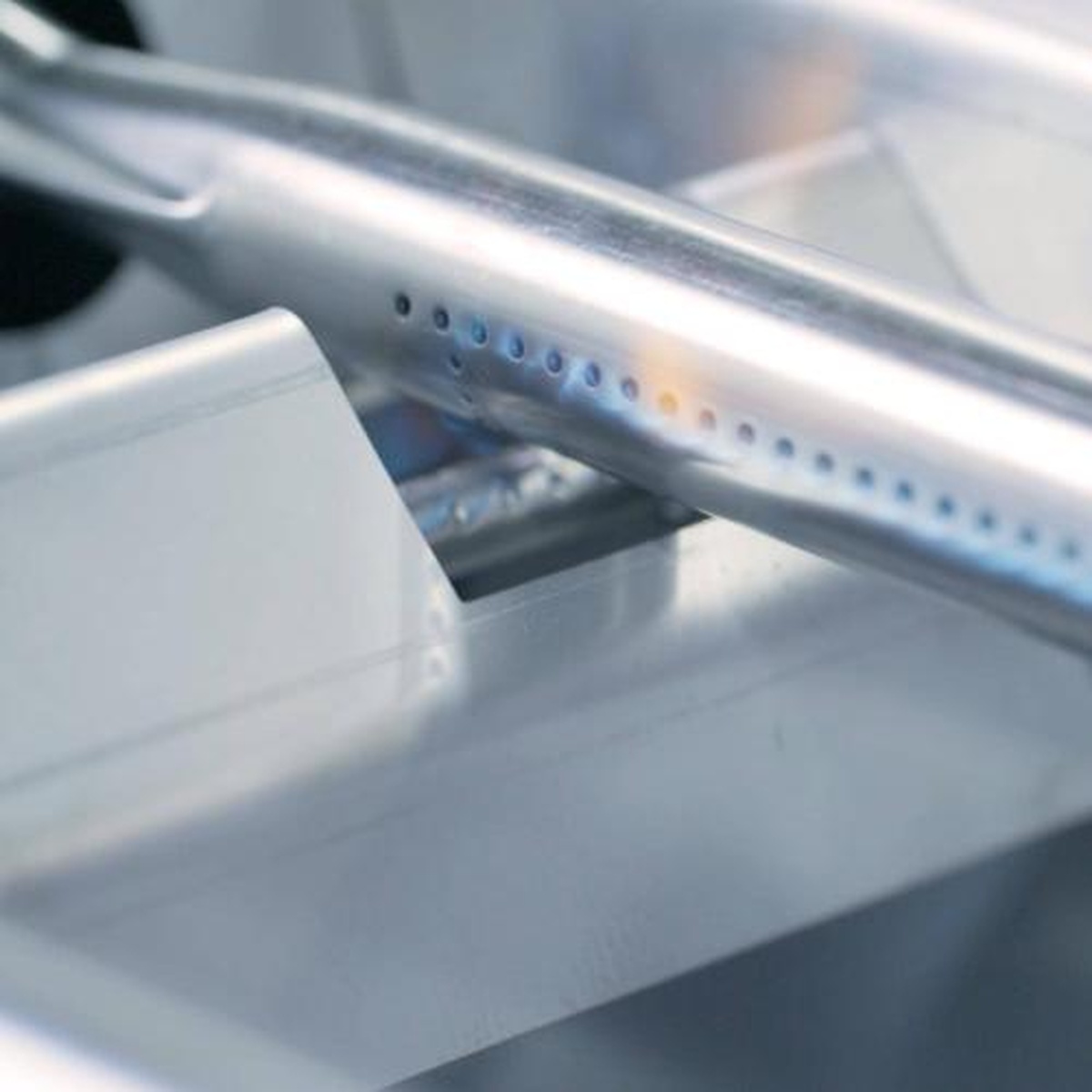 Close-up of stainless steel burner tube and ignition flame on the Crown Verity griddle