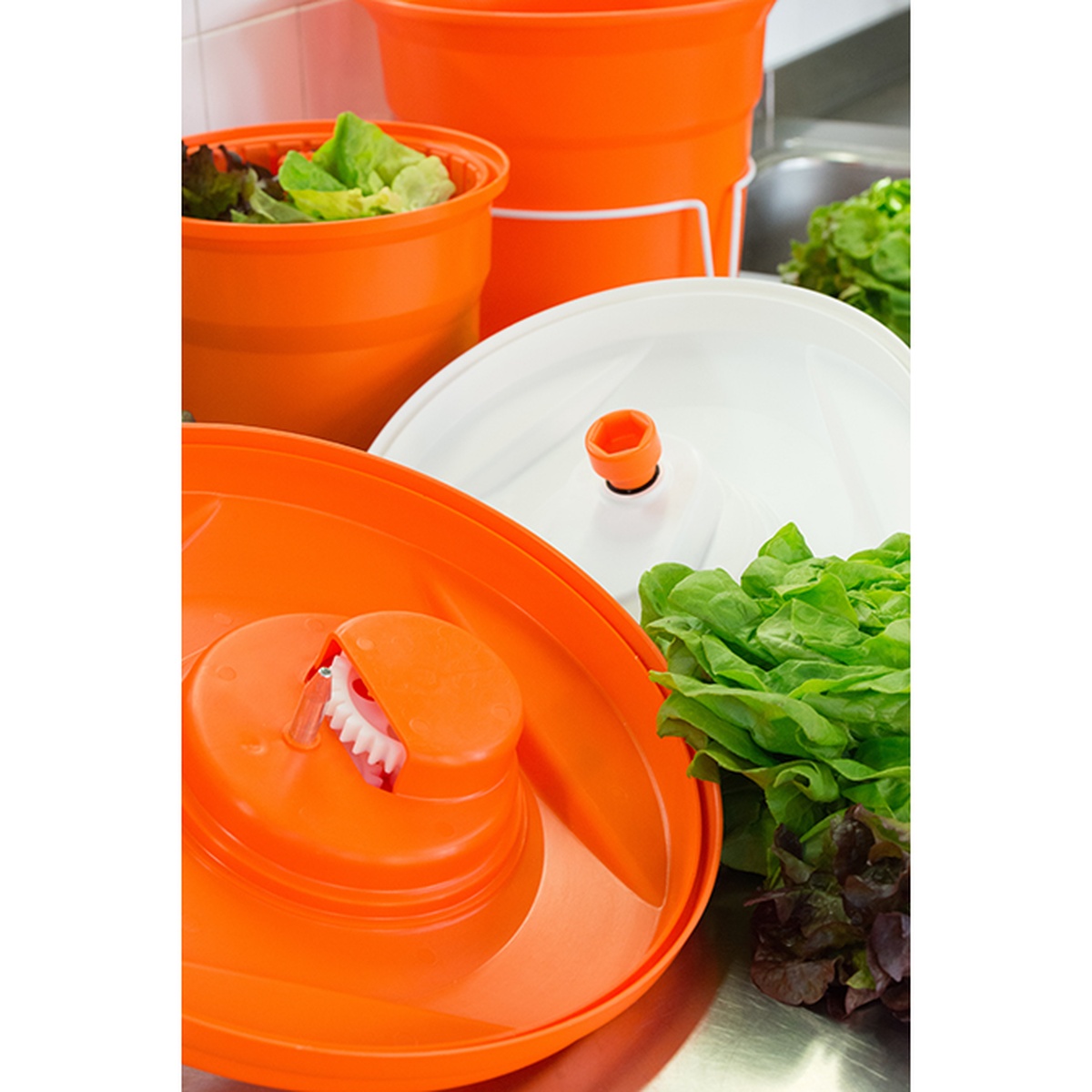 Salad spinner components showing inner basket with lettuce, white top with crank mechanism, and orange bowl