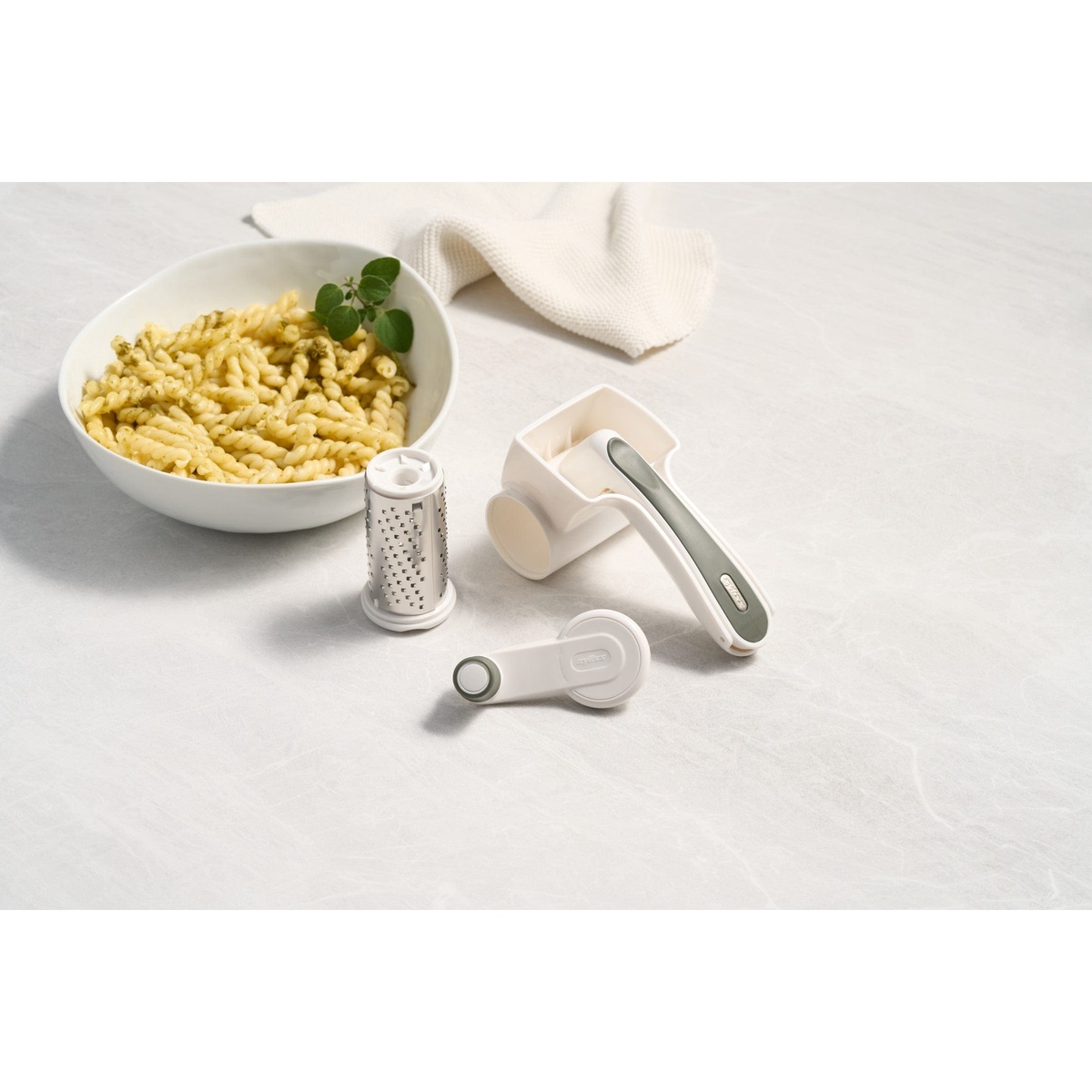 Zyliss Professional Cheese Grater fully disassembled into drum, body, handle, and knob components laid out next to a pasta bowl