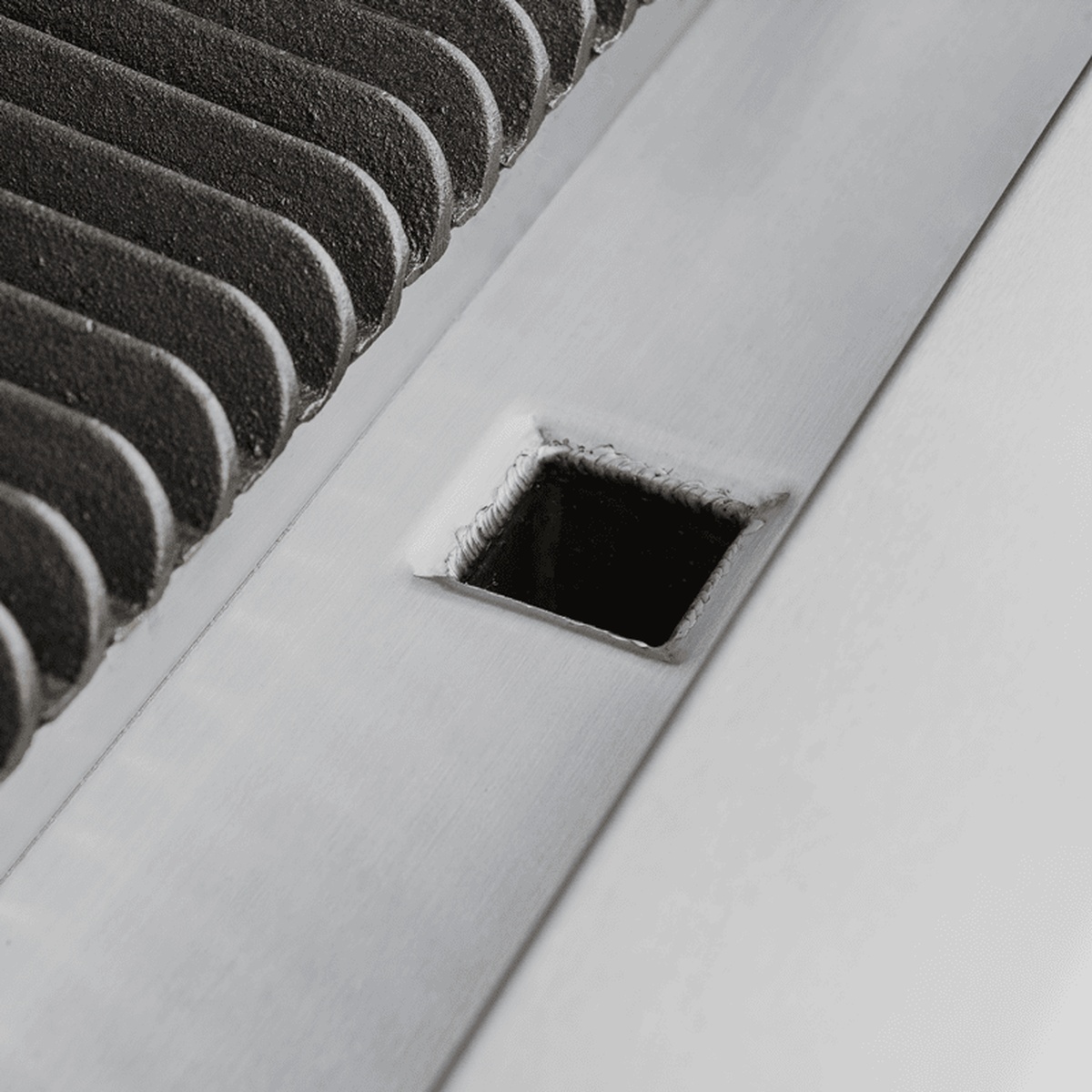 Close-up of EHDCB-48 charbroiler stainless steel grease drain opening beside cast iron grate edge