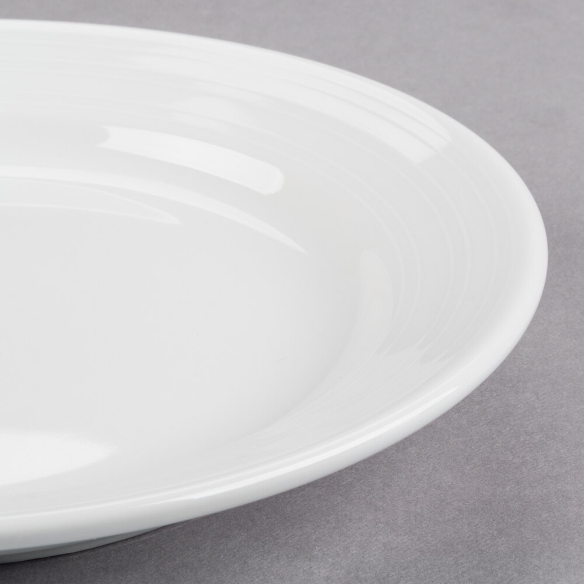 Close-up detail of Tuxton Pacifica plate embossed rim showing wave-pattern texture and bright white glaze