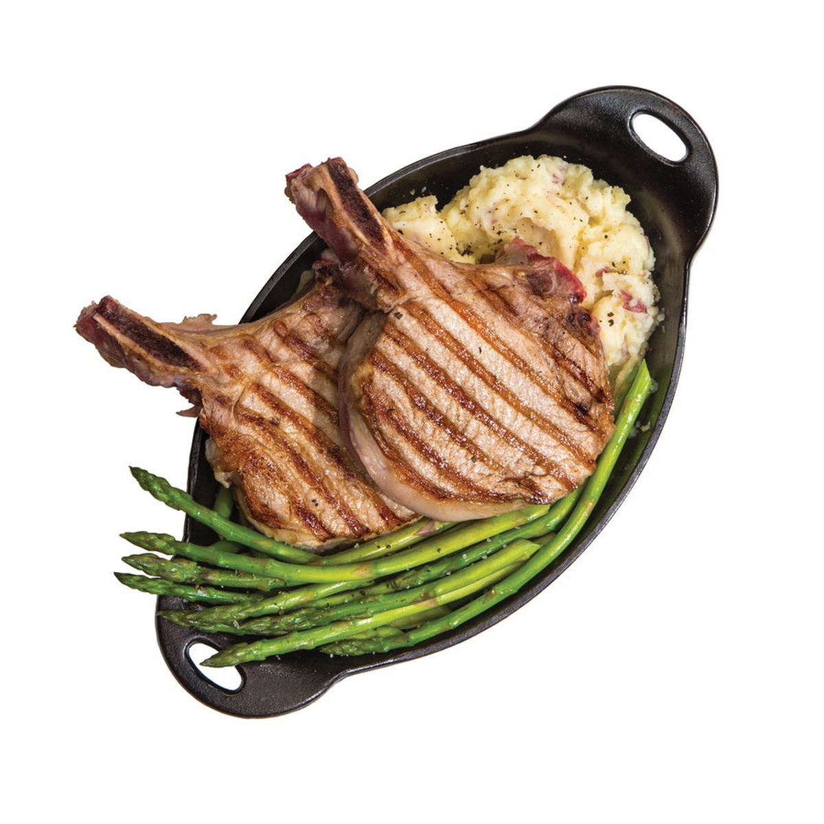 Lodge HOSD oval cast iron server filled with grilled pork chops, asparagus, and mashed potatoes