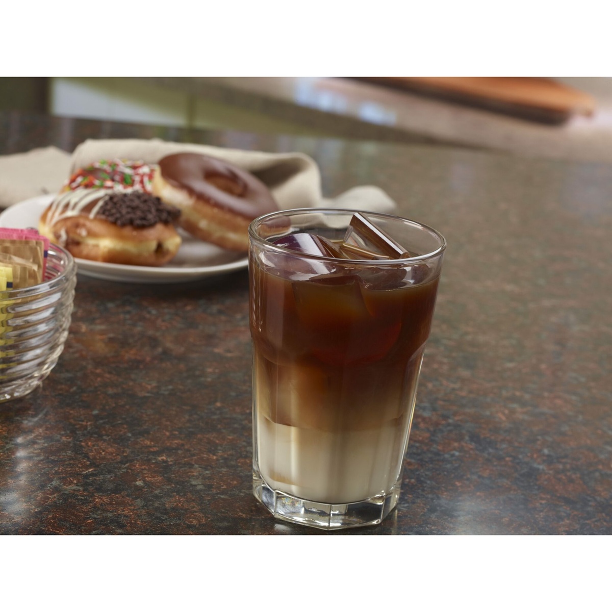 Iced coffee with crescent ice cubes next to a plate of donuts