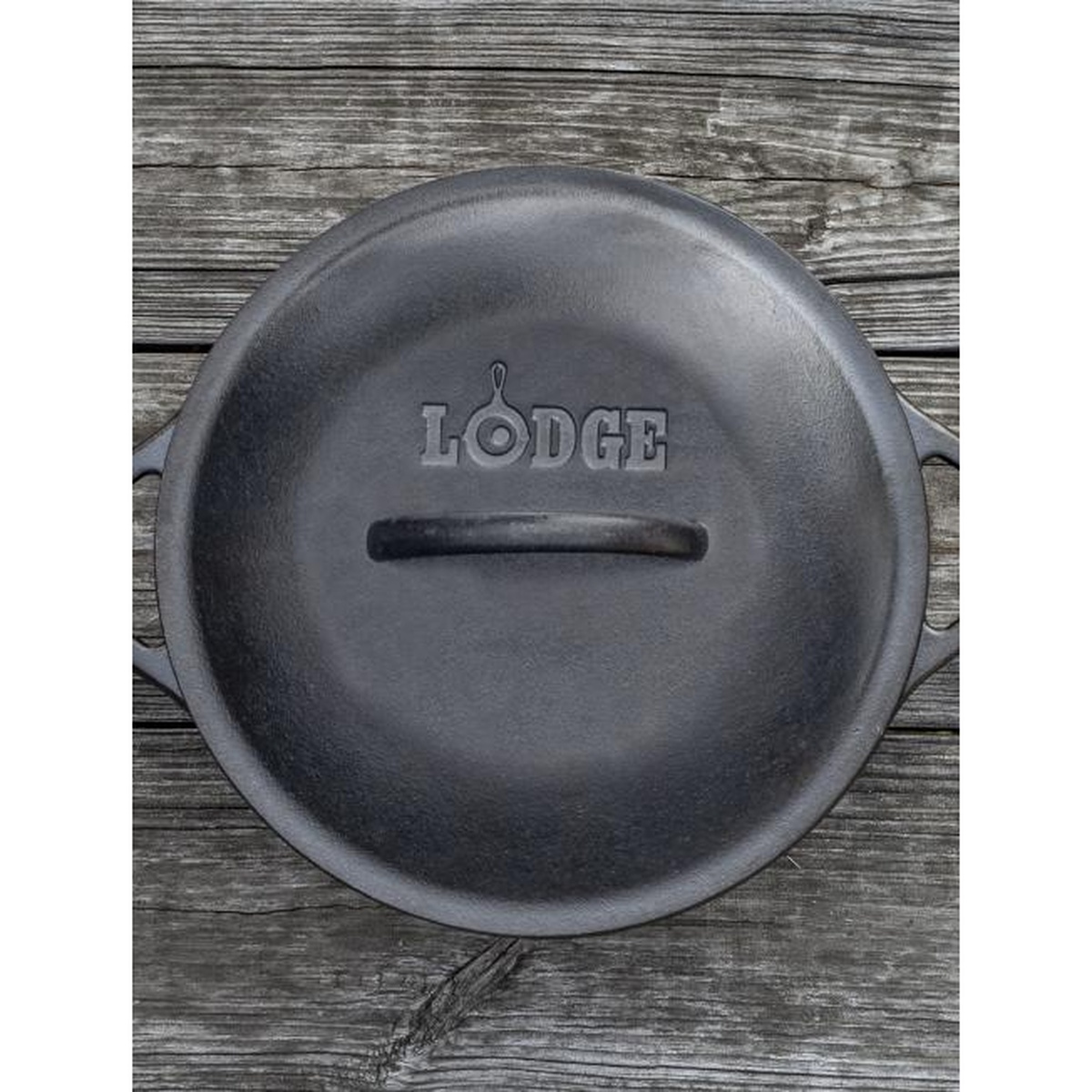 Top-down view of Lodge cast iron Dutch oven lid with embossed Lodge logo on rustic wooden surface