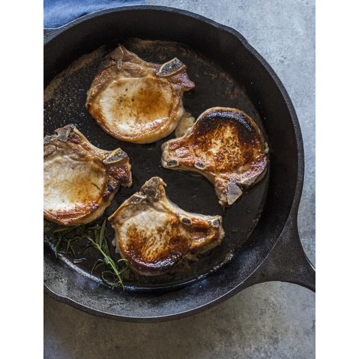 Pork chops cooking in a seasoned cast iron skillet