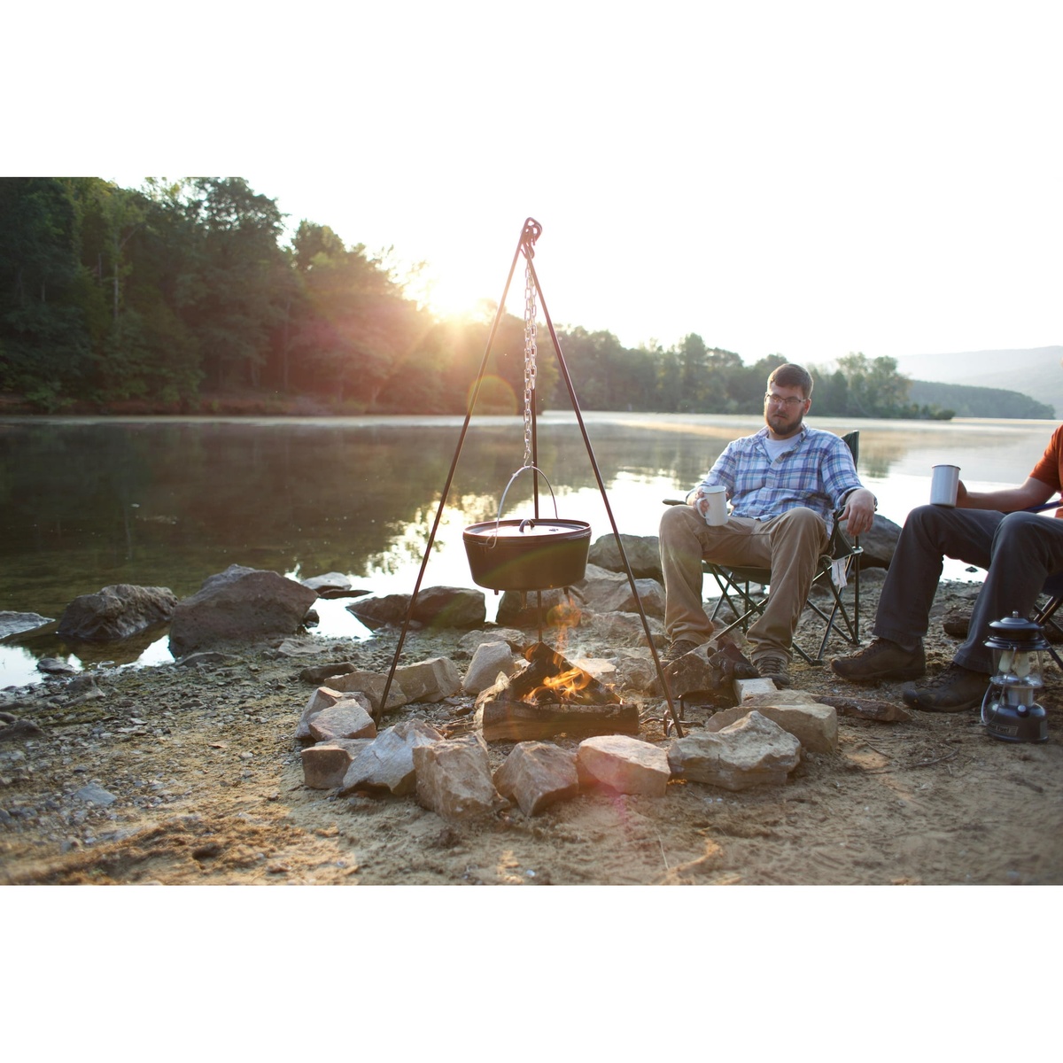 Lodge Dutch Oven hanging from a tripod over a campfire by a lake