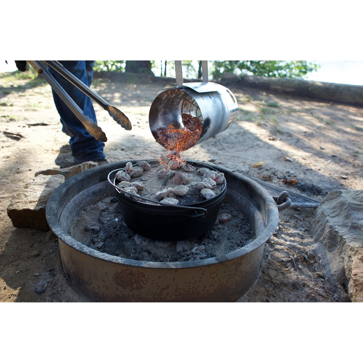 Coals being poured onto the lid of a Lodge Dutch Oven in a fire pit