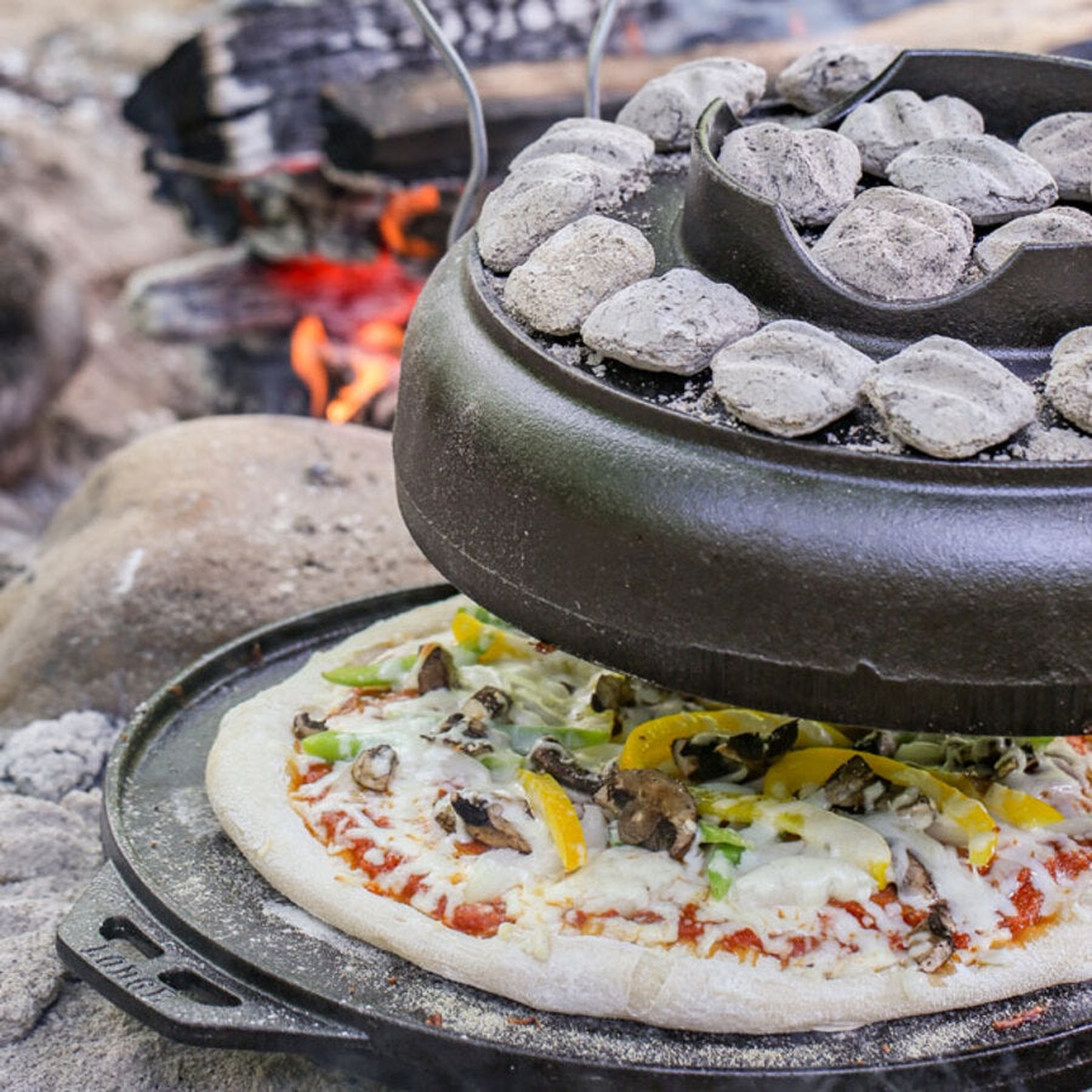 Lodge Cook-It-All used as a pizza oven outdoors with charcoal briquettes on top of the wok lid over a campfire