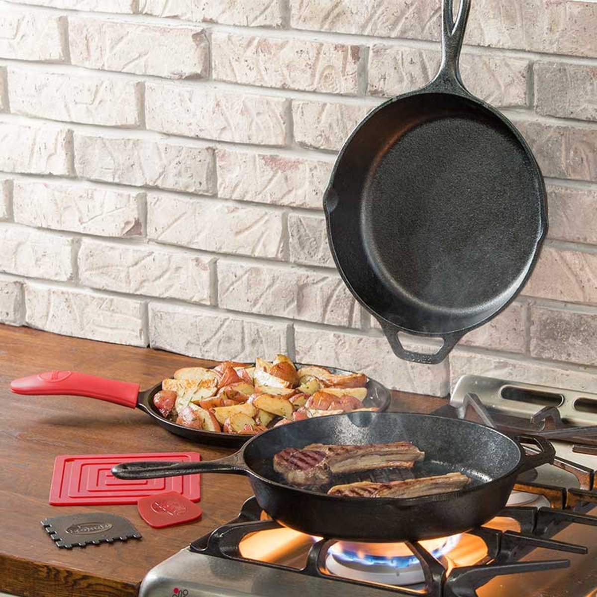 Lodge cast iron pans in use on a stovetop cooking meat and potatoes