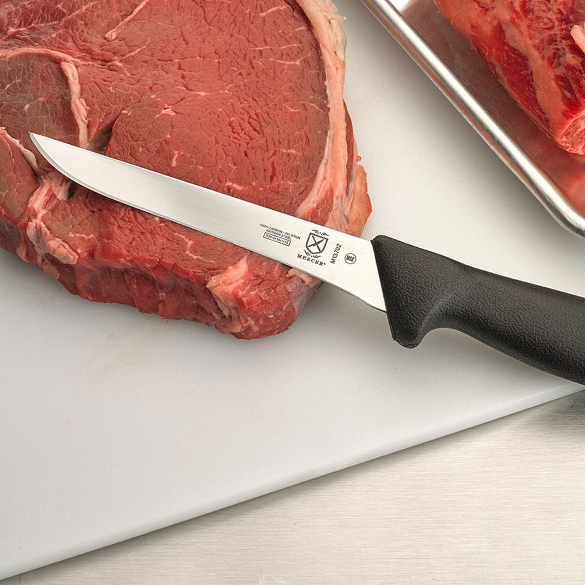 Mercer BPX boning knife resting on a large cut of raw meat