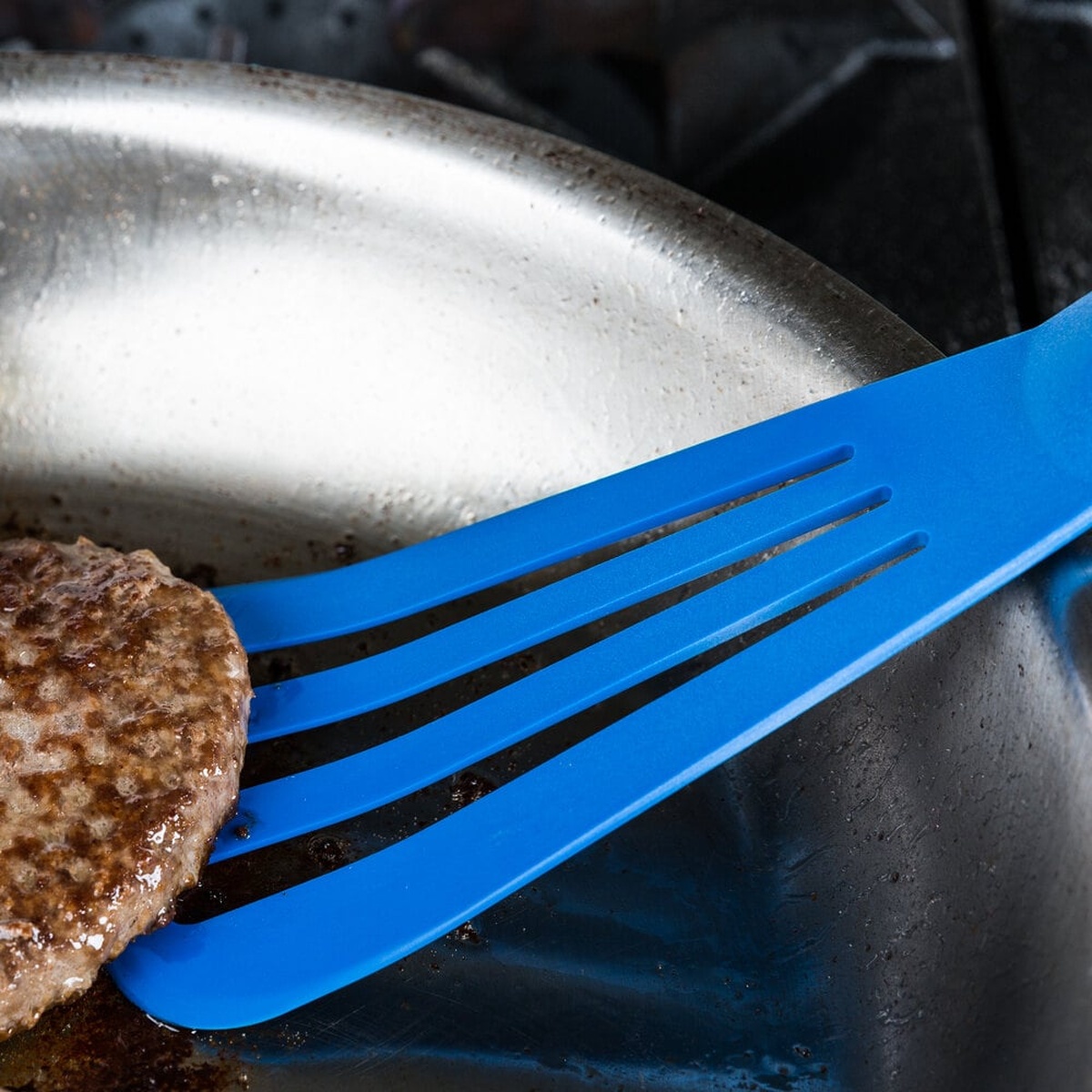 Mercer Culinary blue slotted turner flipping a burger patty in a hot pan
