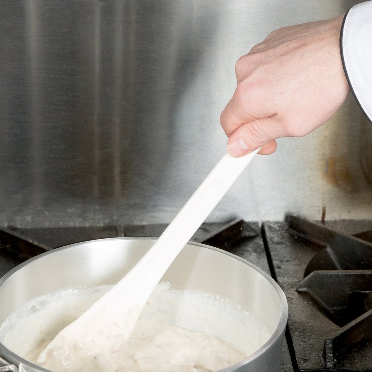 White high temperature spootensil stirring a creamy sauce in a stainless steel pot on a commercial stove