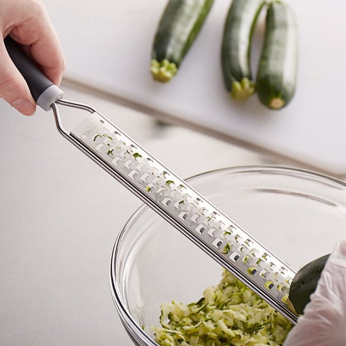 Mercer Culinary extra coarse grater being used to shred zucchini into a glass bowl