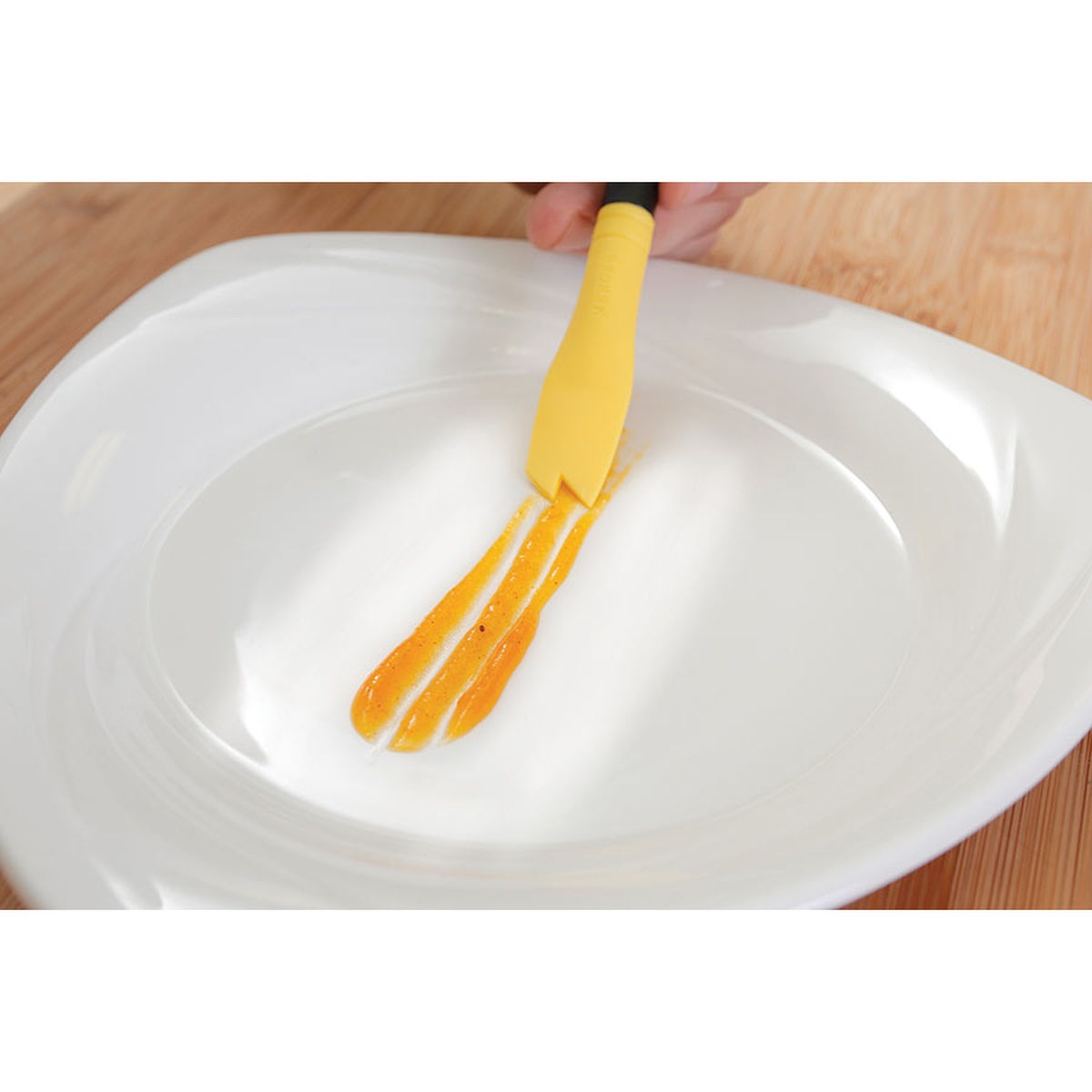 Chef using the yellow saw tooth brush to create thick sauce lines on a white plate
