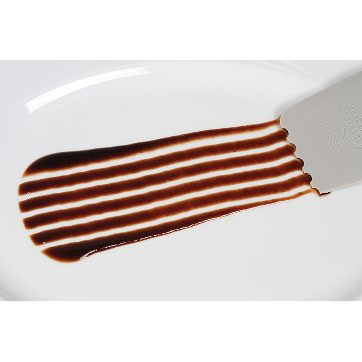 Mercer Culinary M35608 plating wedge creating evenly spaced parallel stripe pattern with dark sauce on a white plate