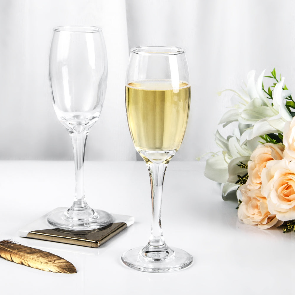Two Enhanced champagne flutes side by side, one filled with sparkling wine, displayed alongside white flowers