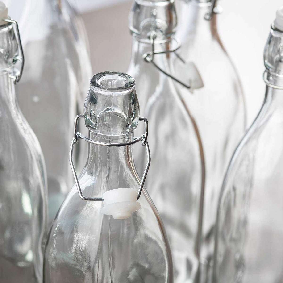 Multiple clear glass swing-top bottles with open bail closures displayed together, showing bottle necks and wire mechanisms