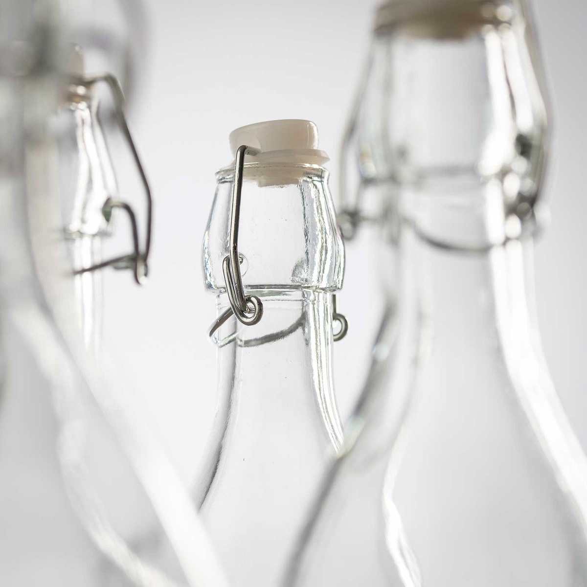 Close-up detail of the swing-top bail wire closure mechanism and white porcelain stopper on a clear glass bottle