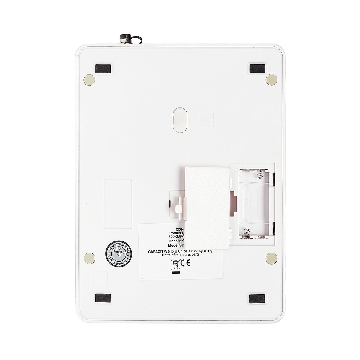 CDN SD0502 scale bottom view showing non-slip rubber feet, open battery compartment for two AAA batteries, and capacity label reading 5 lb at 0.1 oz and 2.27 kg at 1 g with CE certification mark