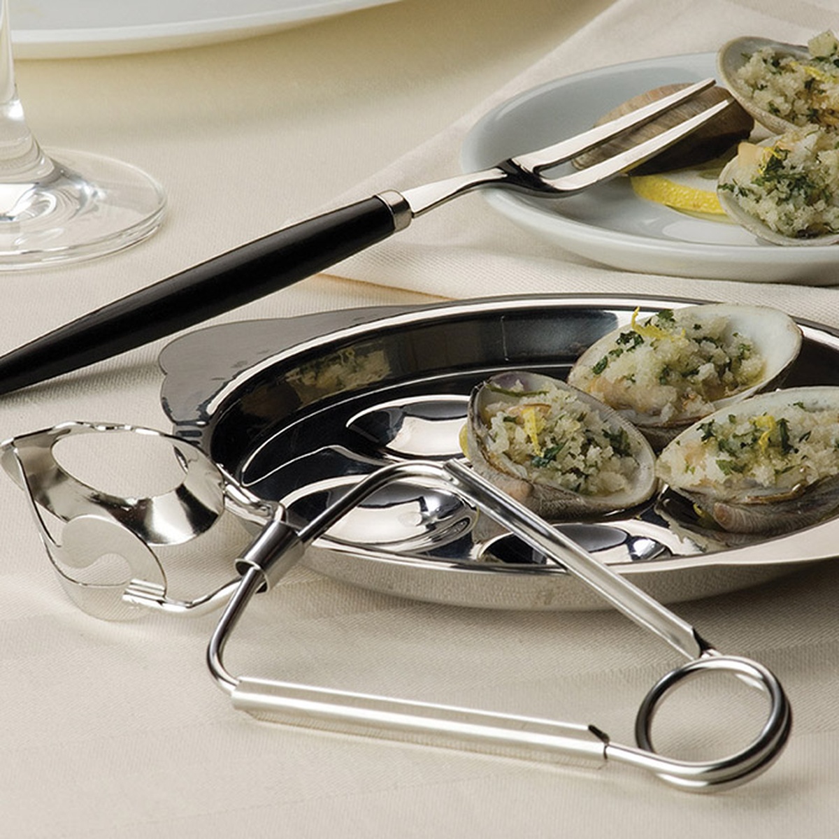 American Metalcraft SNF700 stainless steel snail fork with black handle alongside snail plate and tongs