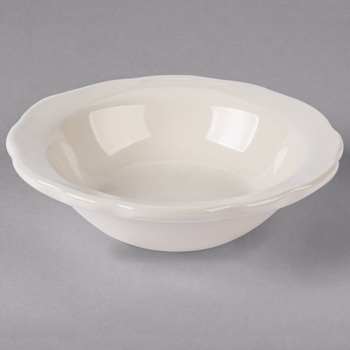 Tuxton TSC-010 Shell 8 oz. eggshell scalloped edge china grapefruit bowl shown from a three-quarter angle on a gray background
