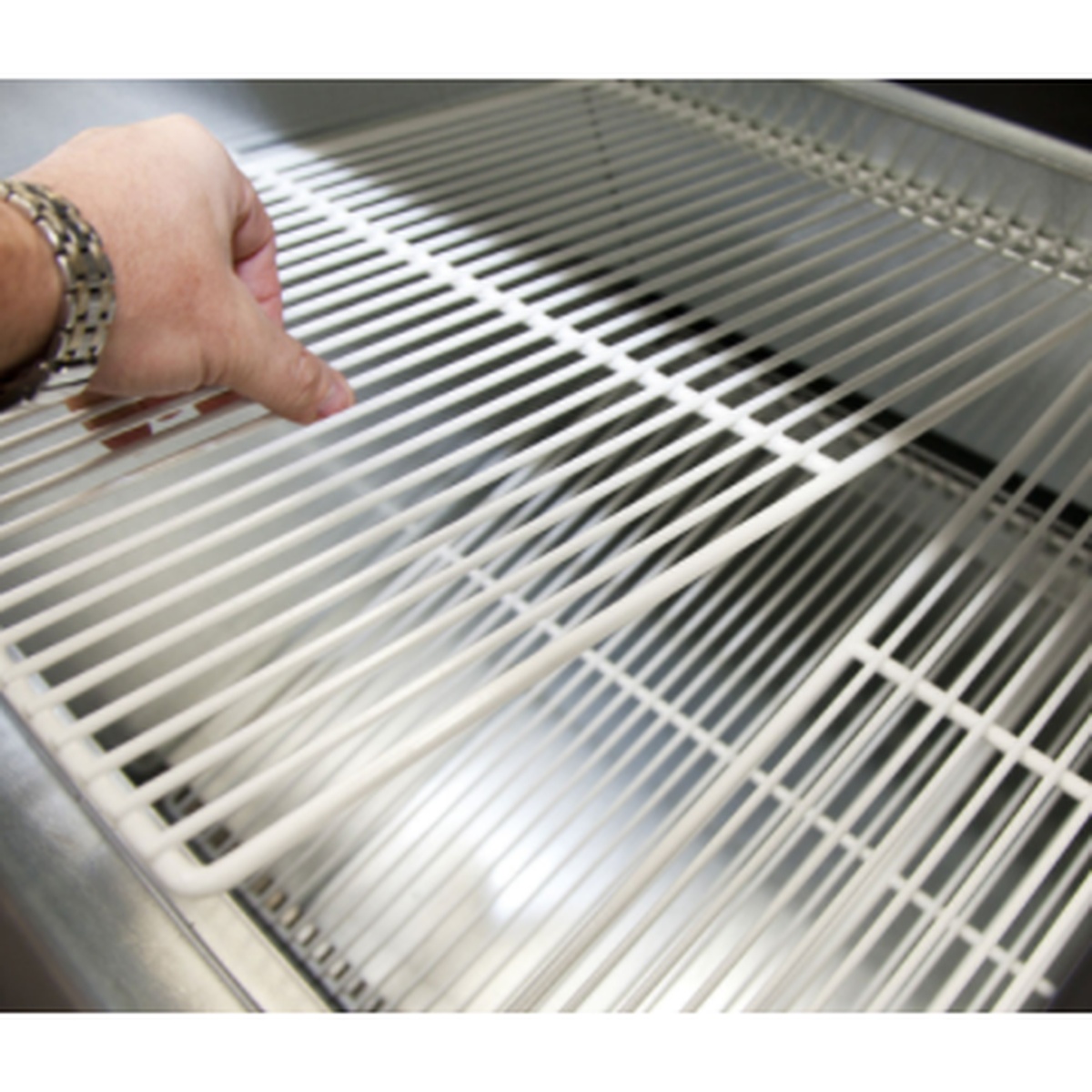 PVC-coated wire shelf being placed into a refrigerated cabinet