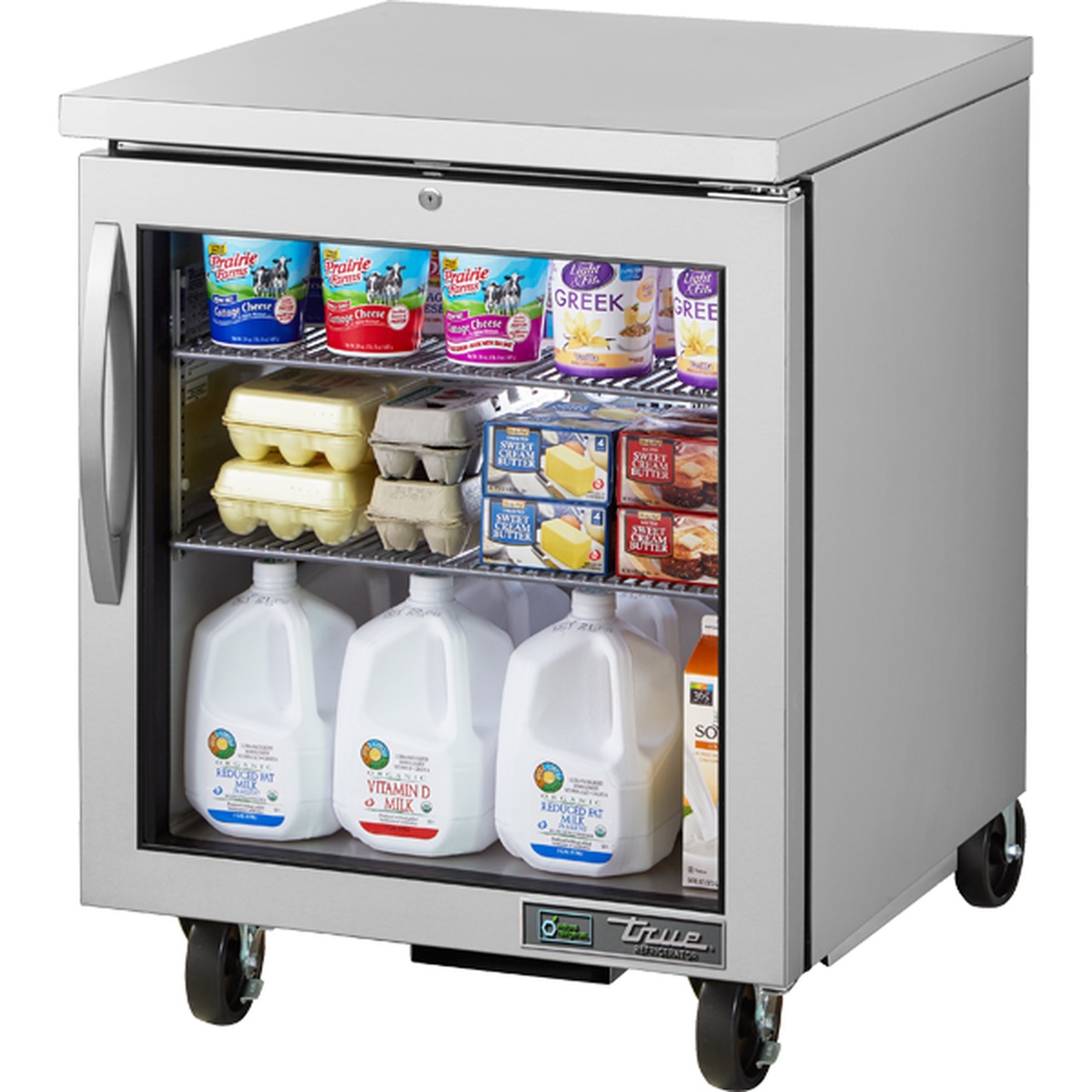 True TUC-27G-HC~FGD01 undercounter refrigerator with glass door, stocked with dairy products on wire shelves, mounted on casters