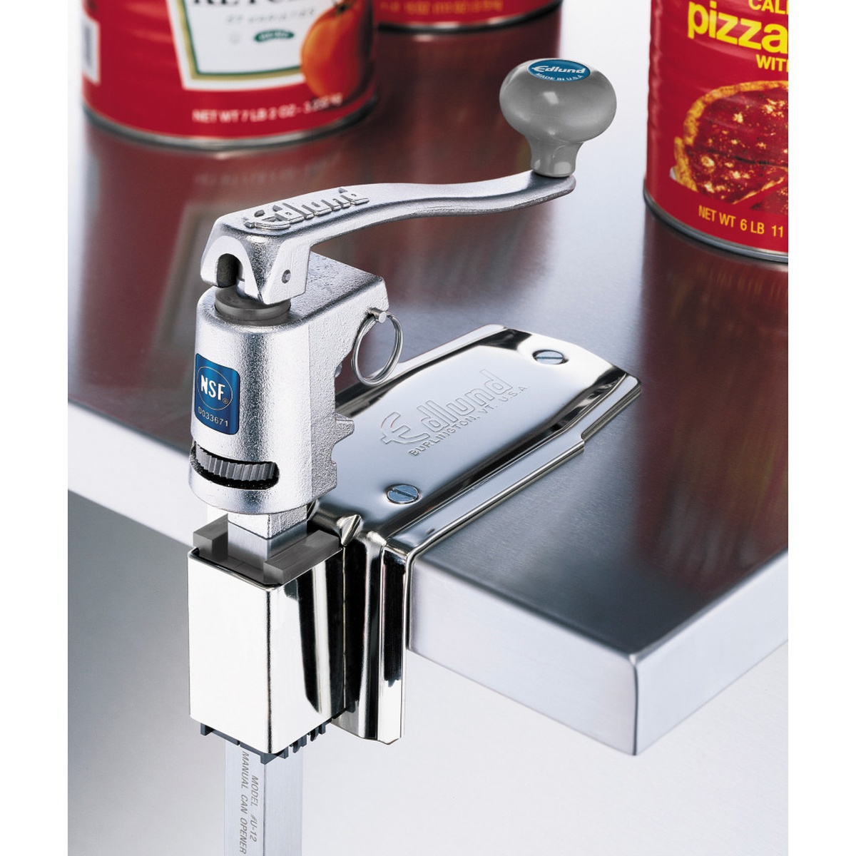 Edlund U-12 manual can opener mounted on a stainless steel counter edge, showing NSF badge, plated base, and adjustable bar