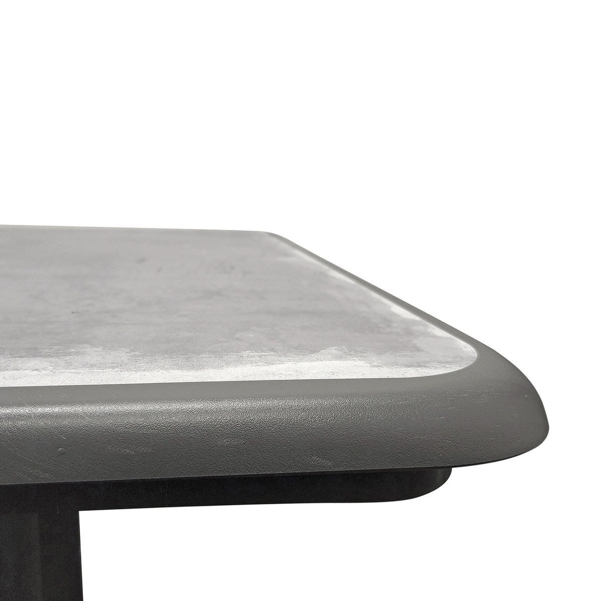 Close-up of Aquaba 32-inch square table corner showing zinc textured surface and rounded resin edge in charcoal