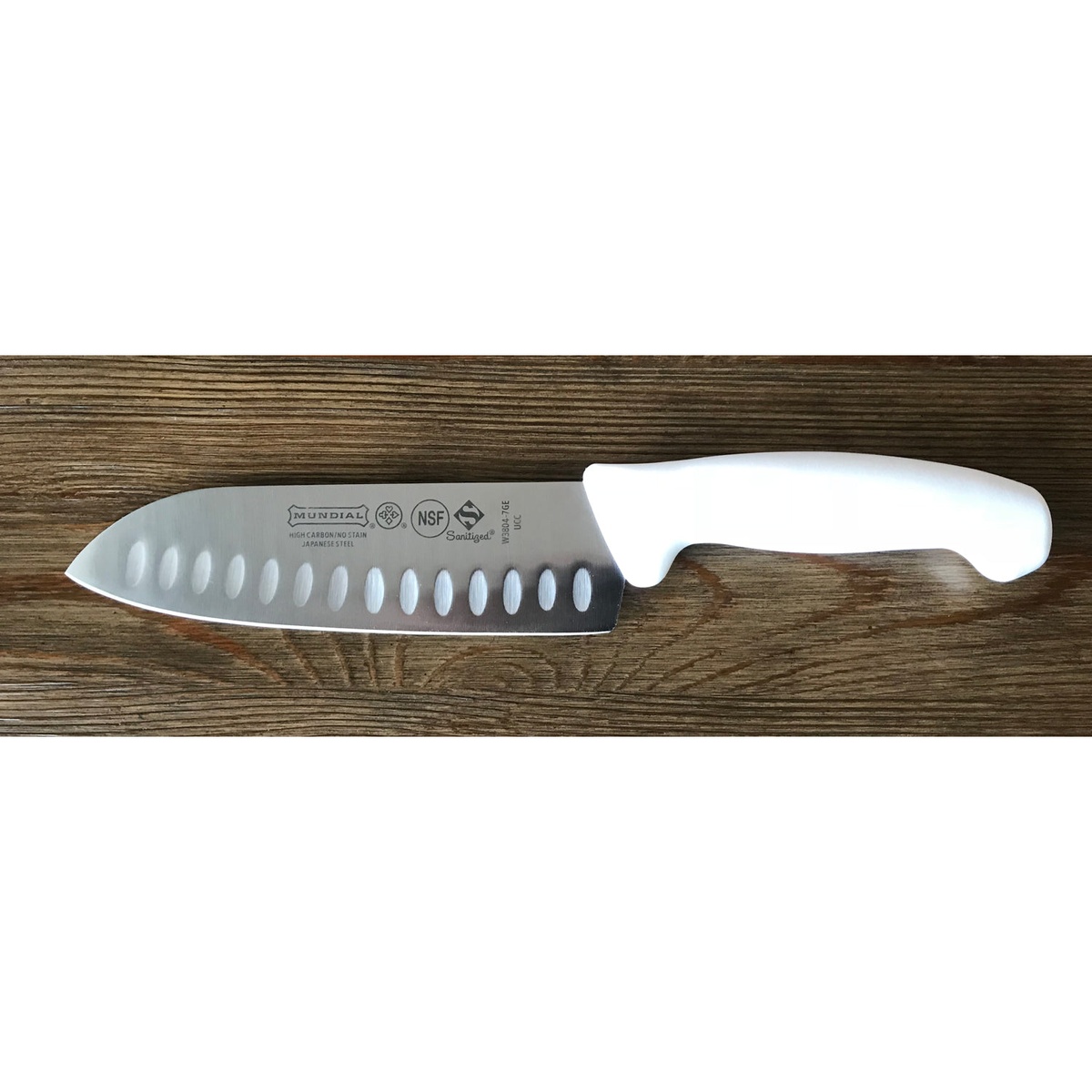 Mundial W3804-7GE 7-inch Santoku knife with white polypropylene handle and hollow edge blade on wooden surface