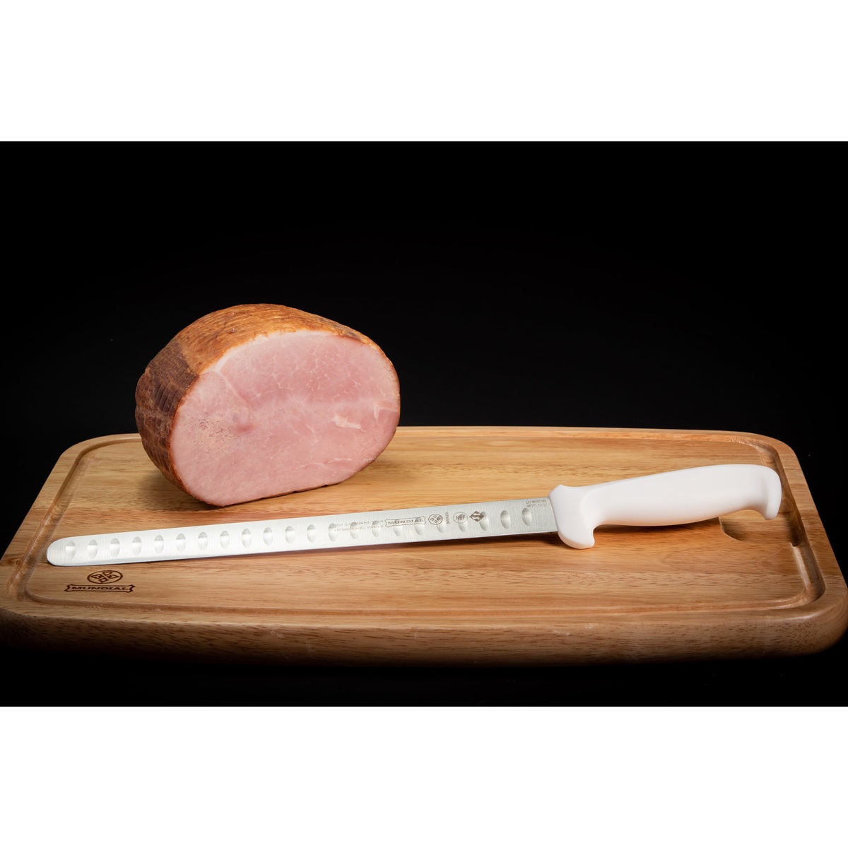 Mundial 12 inch slicing knife on a wooden cutting board next to a large ham