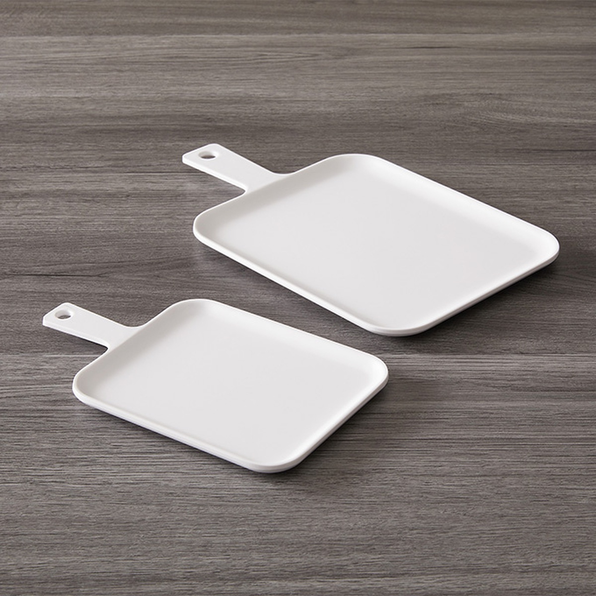 Two white melamine serving peels of different sizes displayed on a wood-grain surface