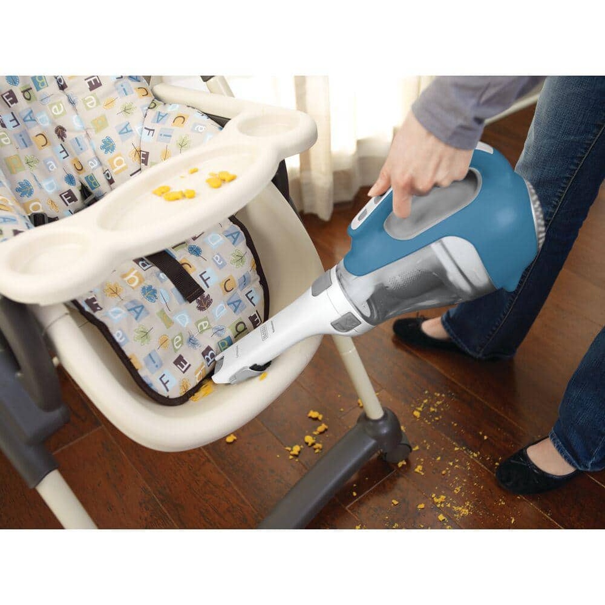 BLACK+DECKER CHV1410L dustbuster handheld vacuum picking up dry food debris around a high chair on a hardwood floor in a kitchen or dining area