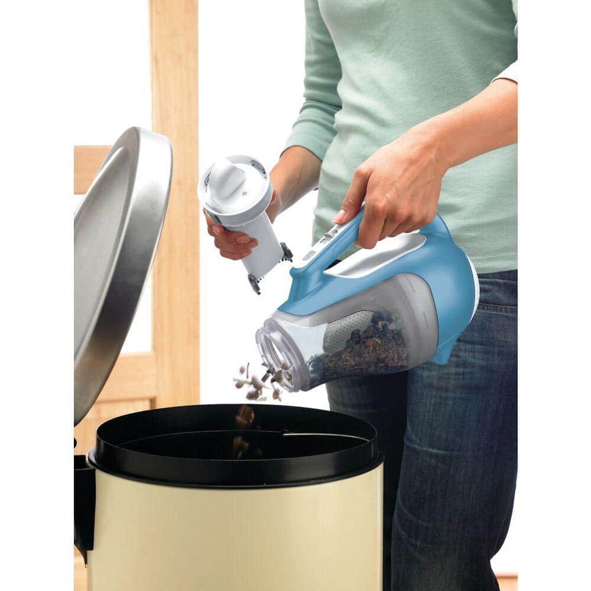 BLACK+DECKER CHV1410L dustbuster handheld vacuum with translucent bagless dirt bowl being emptied into a trash can after household cleanup