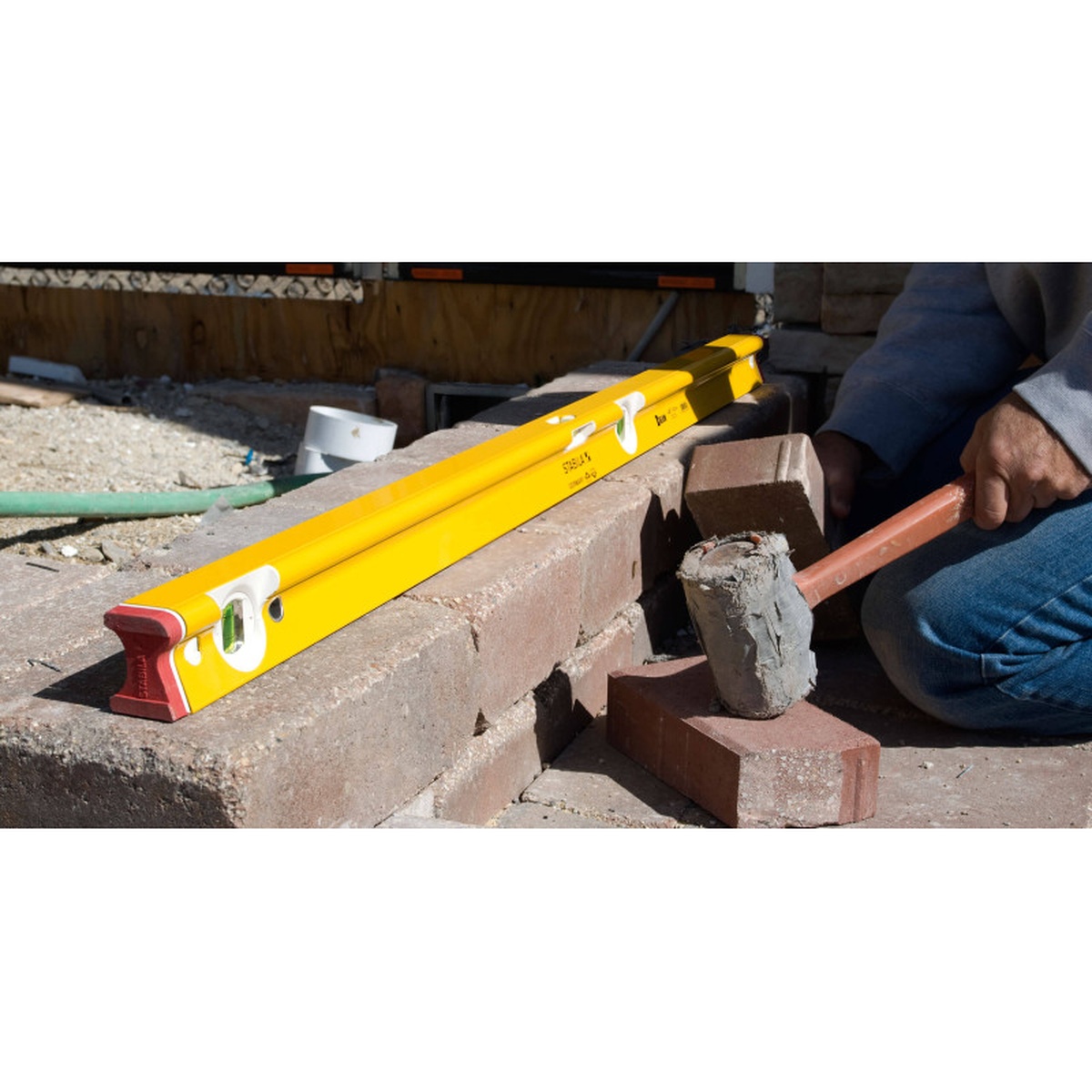 Stabila 41024 24 in R-Beam Level checking level across masonry blocks on an outdoor jobsite during hardscape and construction layout work