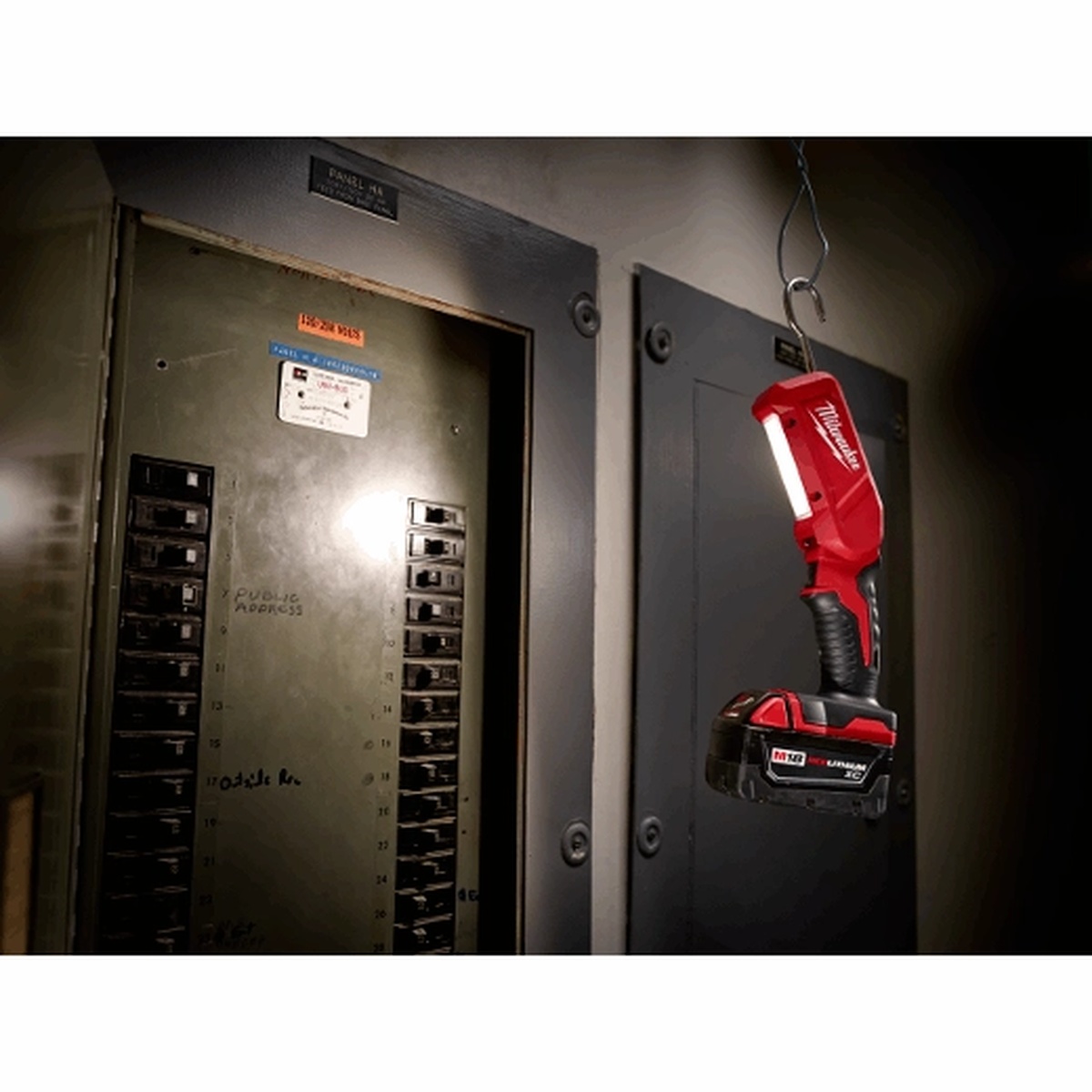 Milwaukee M18 Stick Light hanging from an electrical panel area to provide cordless task lighting during service work in a dark utility space