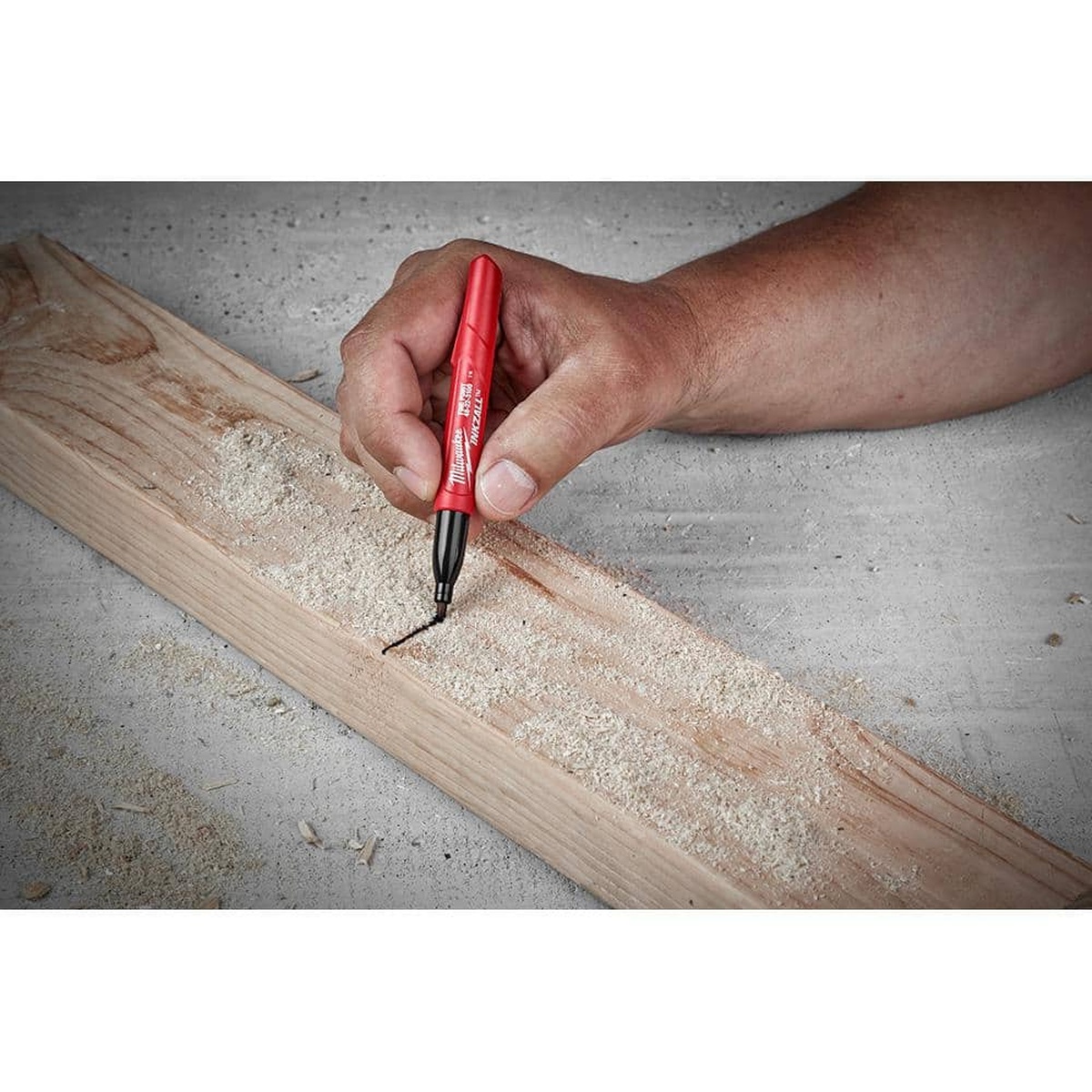 Milwaukee INKZALL Black Fine Point Jobsite Permanent Marker marking a dusty wood board during carpentry layout work on a jobsite