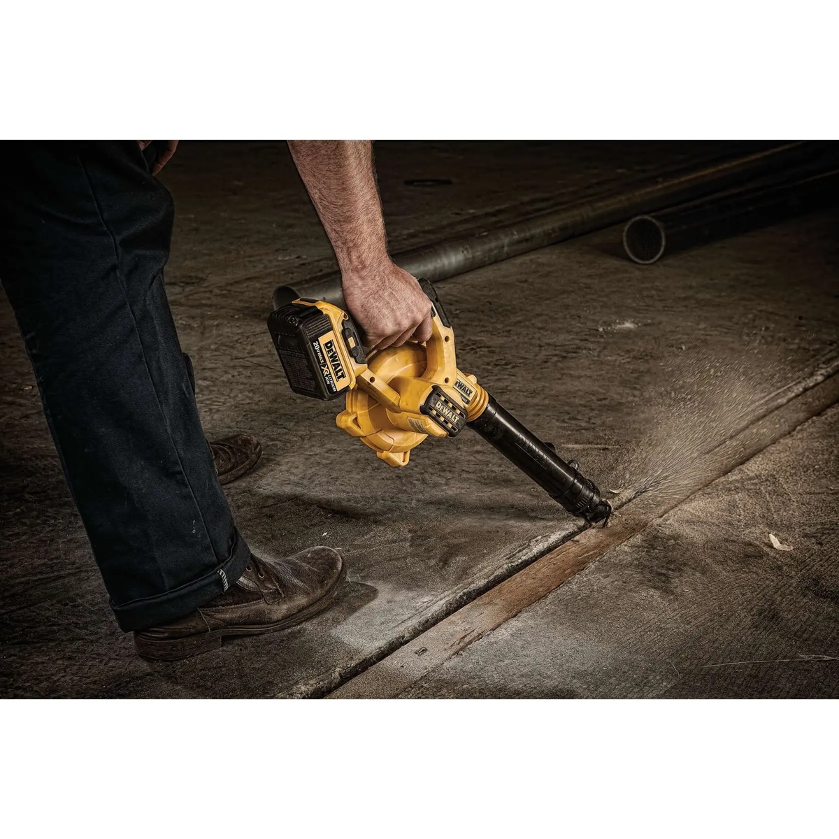 DEWALT DCE100M1 20V MAX Cordless Jobsite Compact Blower Kit using a focused nozzle to clear debris from a concrete expansion joint on a worksite floor