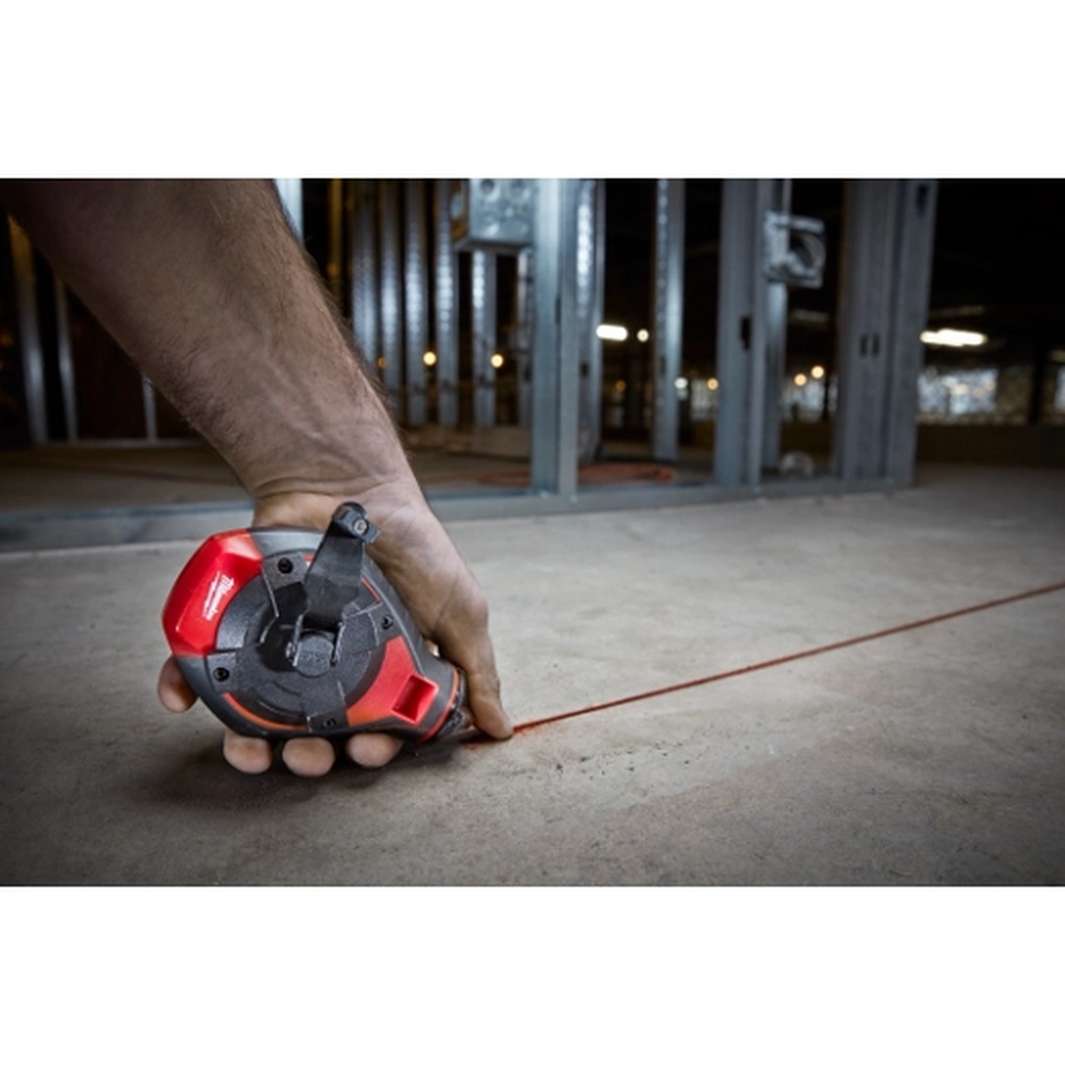 Milwaukee 48-22-3986 chalk reel snapping a red layout line across a concrete floor in a steel stud construction setting