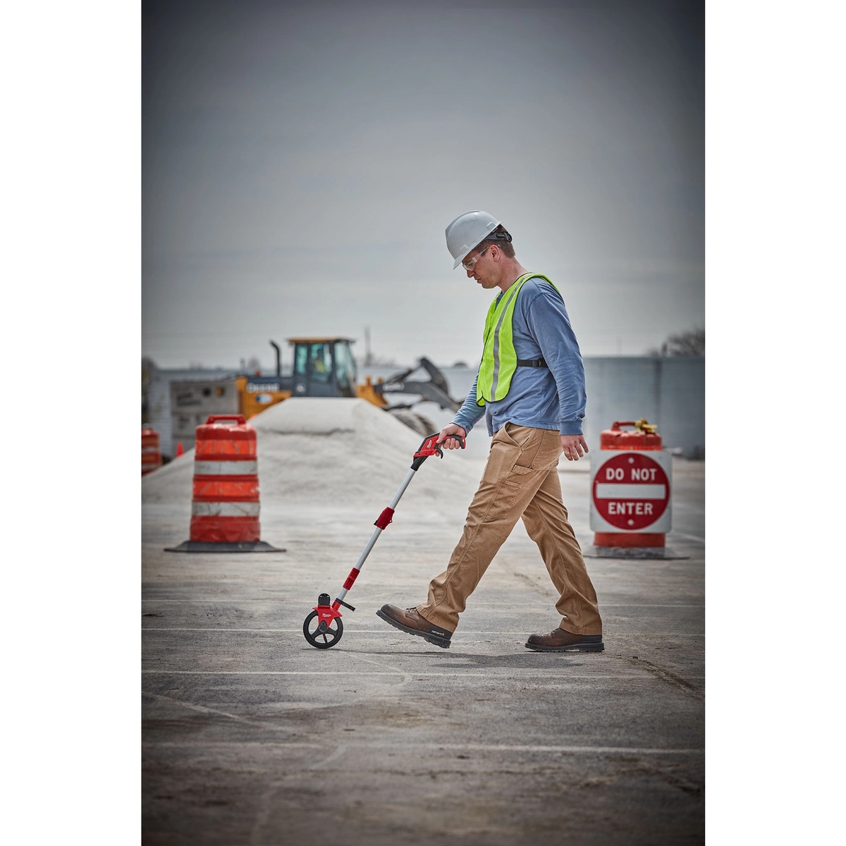 Milwaukee 48-22-5006 6 Inch Measuring Wheel being used on a construction site to measure distance across pavement during layout work