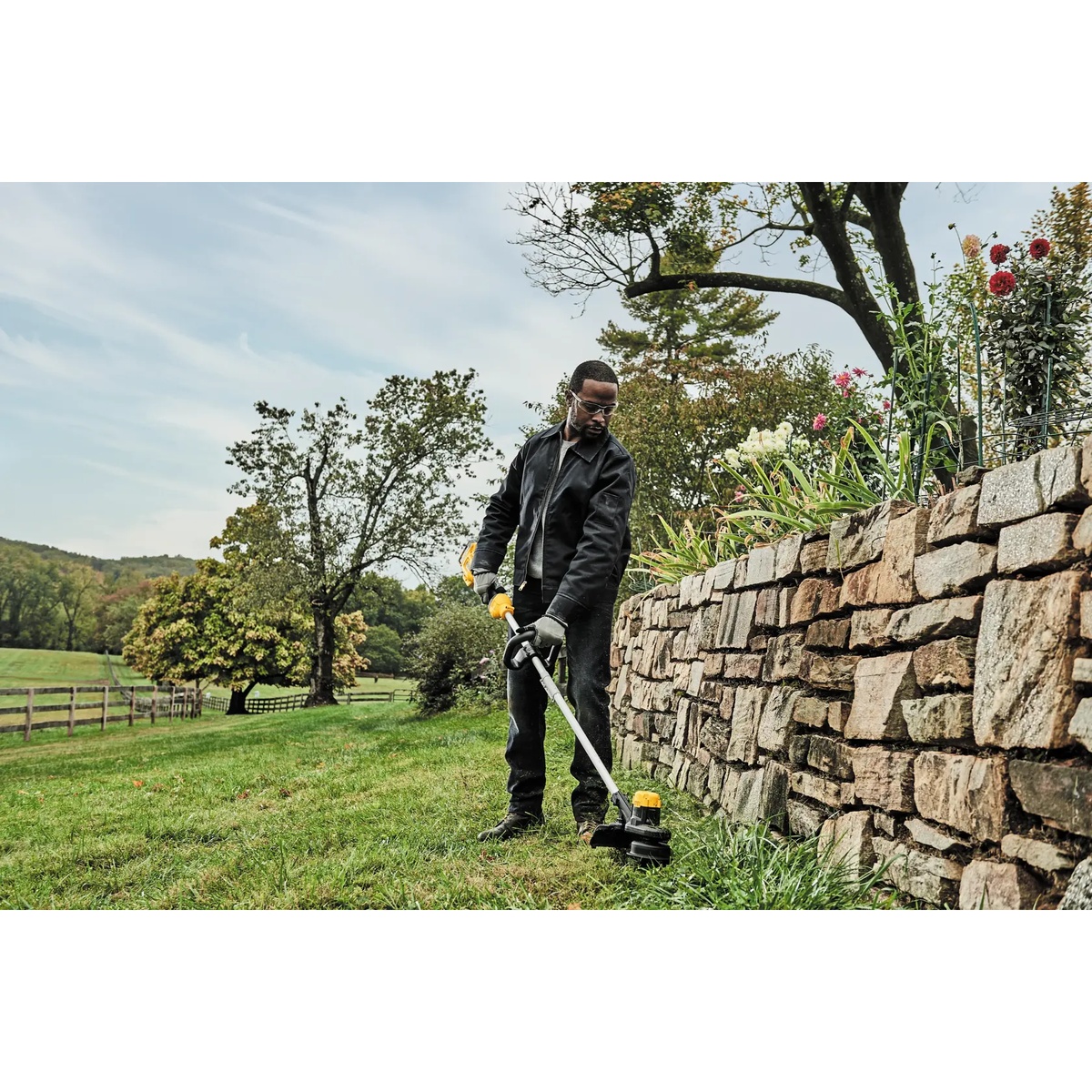 DEWALT DCST925M1 20V MAX 13-In. Cordless String Trimmer Kit trimming grass along a stone retaining wall in a residential yard maintenance setting