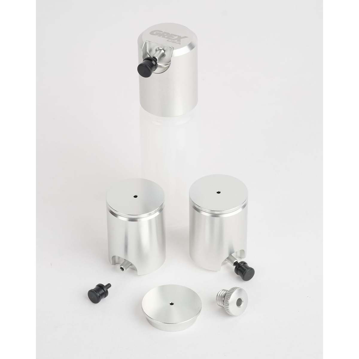 Grex CP05-SS Airbrush Side Cup Set components with multiple aluminum side cups, lids, plugs, and adapter arranged for airbrush painting setup on a workbench