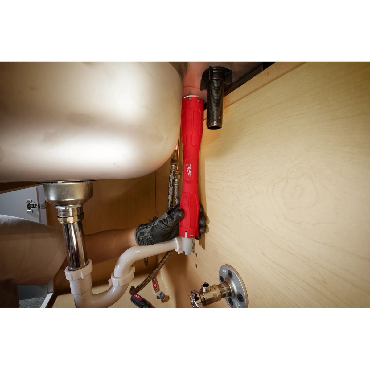 Milwaukee Faucet Swap-Out Wrench reaching behind plumbing hardware under a bathroom sink cabinet during faucet replacement work
