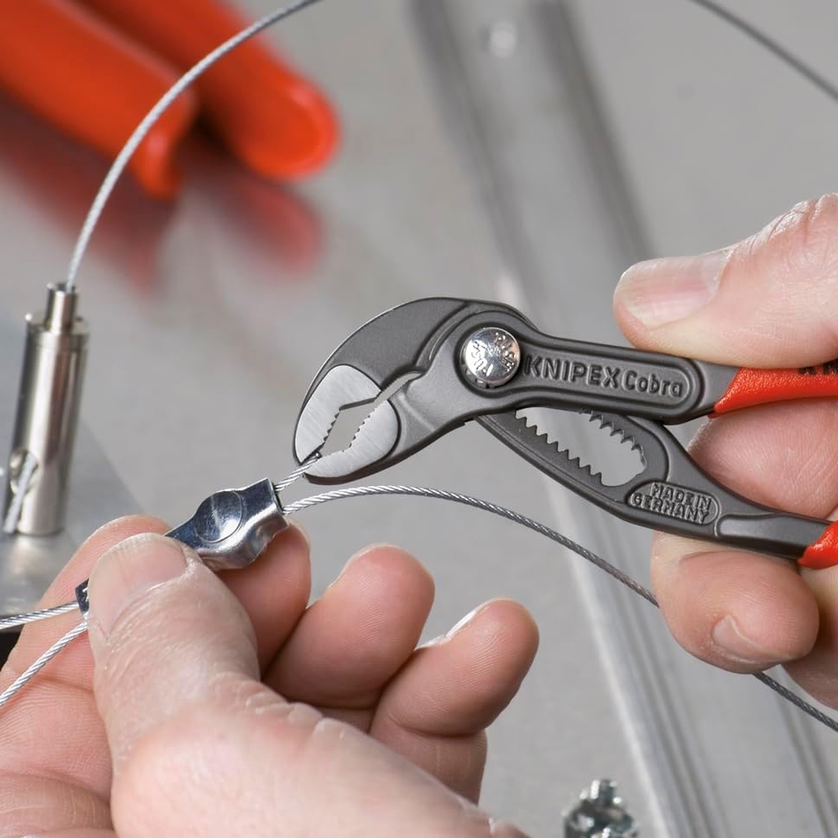 Knipex 87 01 125 SBA 5 in. Cobra Water Pump Pliers gripping a small cable fitting during fine assembly work on metal hardware in a tight bench setup