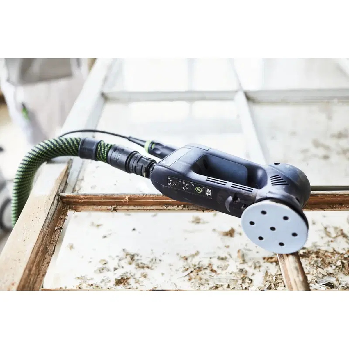 Festool Granat D90 P60 GR/50 sanding disc mounted on a Festool RO 90 DX detail sander connected to dust extraction while sanding a painted wood frame on a jobsite