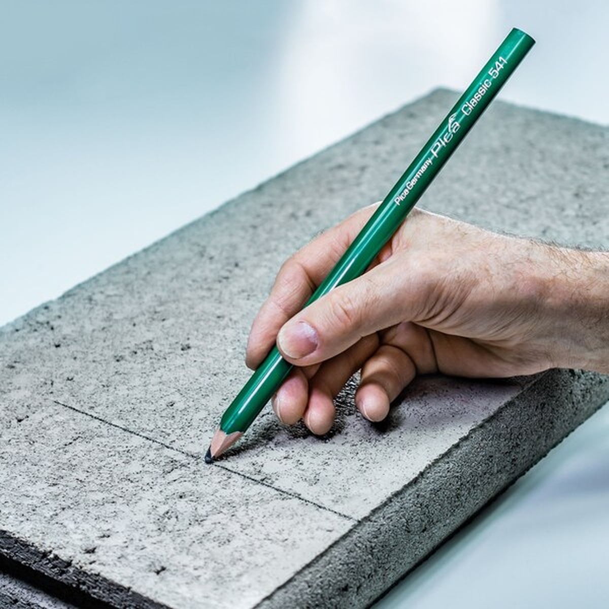 Pica 541/24 Green Stonemason Pencil marking a concrete slab during masonry layout work on a dry jobsite surface